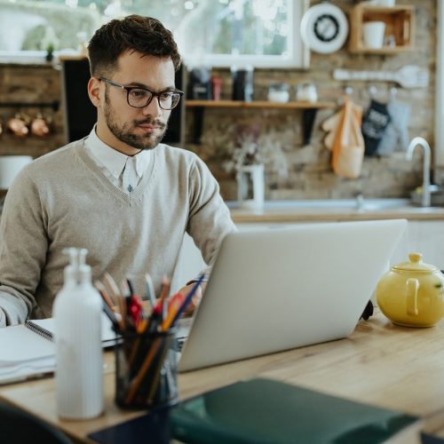 Young freelancer working on a computer while going through paperwork at home.